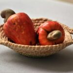 Close-up of ripe cashew apples in a woven basket on a white surface, perfect for food and natural settings.